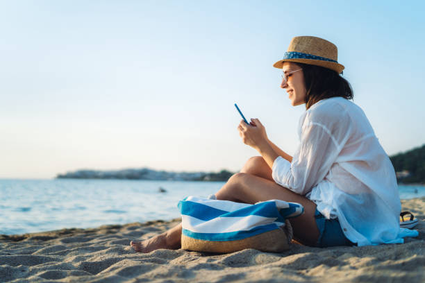 Young beauiful caucasian woman using phone at the beach.